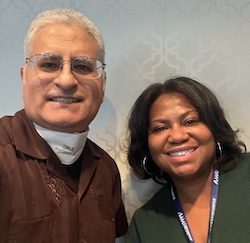 Photo of speakers (from left to right) Alberto Roca and Chloe Poston both smiling at camera. Roca has short gray hair and glasses while wearing brown "guayabera" button shirt. Poston has sholder length black hair and hoop earrings while wearing dark green dress.