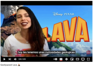 Screenshot from GeoLchat Geollywood YouTube video where woman with long brown hair wearing white t-shirt is pictured in front of still image from the Disney movie "Lava" with erupting volcano. Closed captioning states (originally in Spanish) "Today we have some geological curiosities for you."