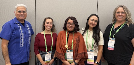 Photo of panelists from "Postdoc Fundamentals" session all standing from left to right Roca, Palominos, Paniagua, Zamora, and Sugiura. Roca is older with gray hair wearing glasses and blue guayabera shirt. Palominos has shoulder-length brown hair and is in a red shirt. Paniagua has shoulder-length brown hair and is wearing glasses and an orange cape-like sweater. Zamora has long brown hair and is wearing a white shirt with buttons. Finally Sugiura has shoulder-length blond hair while wearing glasses and a black blouse.
