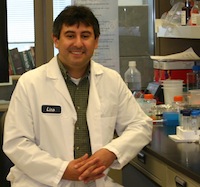 Photo of Lino Gonzalez at his laboratory bench while wearing a white lab coat.